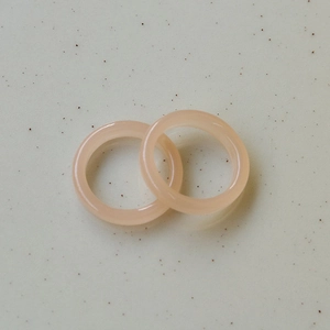 Close-up of two translucent candy-colored resin rings in soft peach pink finish