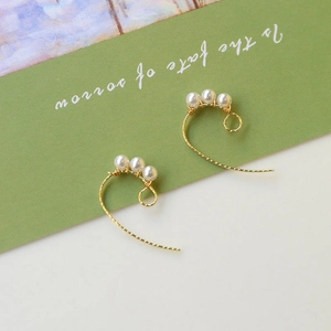 Détail de boucles d'oreilles dorées avec trois perles blanches alignées sur crochets spirale