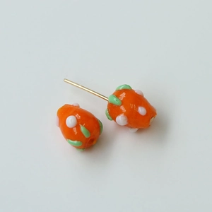 Handmade orange glass stud earrings with green leaf detail and white polka dots