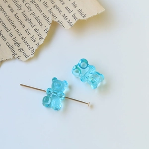 Macro shot of two light blue translucent jelly bear charms with a gold earring pin