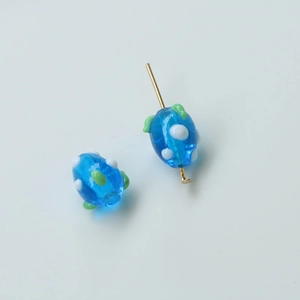 Macro view of blue glass beads with white dots and green leaf accents for DIY jewelry