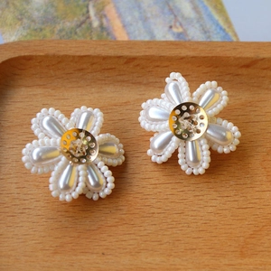 Elegante handgemachte weiße Perlenohrringe in Blütenform mit goldenem Kern auf Holz