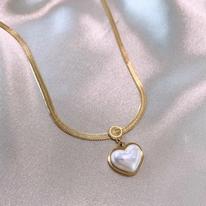 Detailed close-up of golden heart pendant necklace with pearl inlay and Love tag