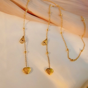 Minimalist gold heart pendant necklace with beaded chain on soft beige silk fabric
