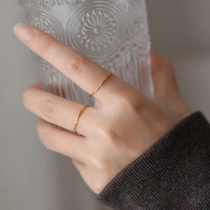 Detail of minimalist gold plated rings with small zircons held by hand on glass