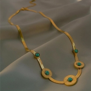 Gold flat snake chain necklace with five turquoise sunburst pendants on silk texture