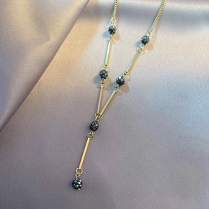Detail of a gold Y-shaped necklace featuring black faceted beads on a silk fabric background