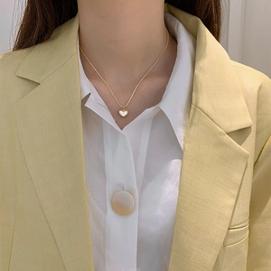 Elegant gold heart pendant necklace with white shell inlay worn by a model in casual outfit