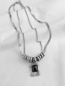 Detalle de collar plateado de doble capa con gema negra y colgante de textura lava