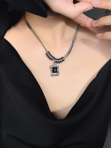 Detalle de un collar de plata con colgante de piedra negra sobre un elegante traje negro