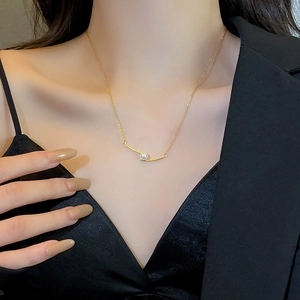Minimalistische parelketting met gouden staaf, close-up op model met diepe V-hals blazer