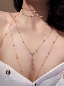 Close-up of gold layered body chain featuring bead necklaces and rhinestone tassels