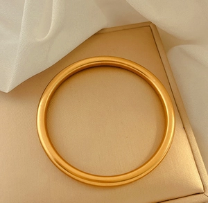 Vista macro di un bracciale rigido in oro opaco con elegante texture satinata