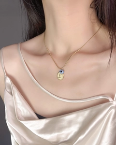 Dettaglio della collana dorata con ciondolo lettera E e occhio blu su catena a serpente
