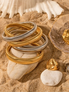 Stack of gold and silver textured stretch bracelets and lava rings on a sandy beach