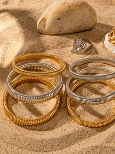 Close-up of gold and silver gas pipe spiral texture bangles on desert sand background