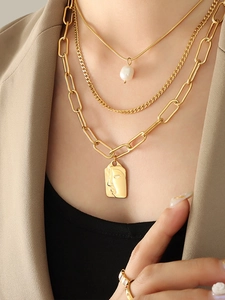Detail of layered gold necklaces with pearl and square face pendant on a model