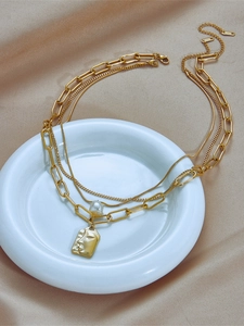 Close-up of triple-layered gold necklace with paperclip chain and portrait medallion