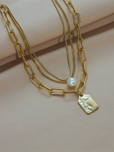 Detailed view of layered gold necklaces with portrait pendant and white pearl charm