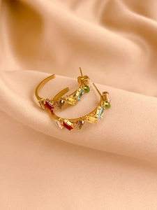 Detail von goldenen C-Ohrringen mit bunten Baguette-Kristallen auf glänzendem Satin