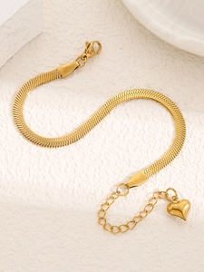 Détail du bracelet chaîne serpent dorée avec pendentif cœur sur texture minérale