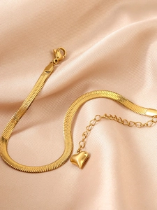 Détail d'un bracelet maille serpent doré avec pendentif cœur sur tissu en soie champagne