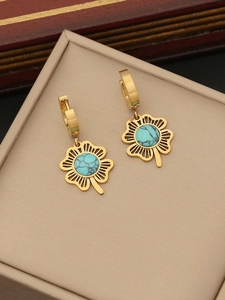 Gros plan de boucles d'oreilles trèfle dorées avec turquoise sur un support beige