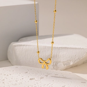 Elegante collana con ciondolo a fiocco dorato e catena a sfere su sfondo di pietra bianca