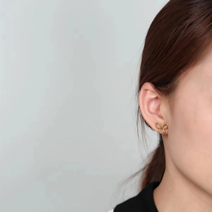 Pendientes de lazo dorado minimalista para mujer mostrados puestos en una modelo real