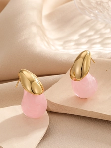 Détail de boucles d'oreilles dorées avec gouttes en résine rose sur pierre beige