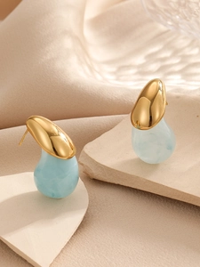 Gros plan de boucles d'oreilles goutte en métal doré et résine bleu clair sur pierre