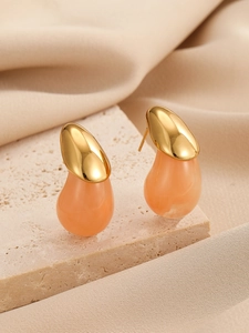 Détail de boucles d'oreilles dorées avec pierres en résine rose sur fond de pierre