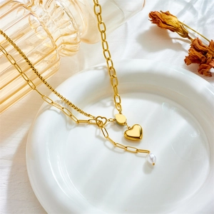 Gold layered heart necklace with white pearl pendant and paperclip chain on white ceramic plate