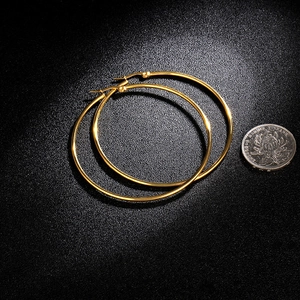 Macro view of large gold-plated hoop earrings with size comparison coin on black background