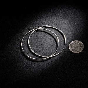 Detailed comparison of large silver metal hoop earrings with a coin for size reference