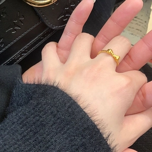 Détail d'une bague nœud en plaqué or 18 carats portée au doigt sur fond noir élégant