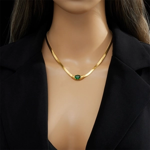 Gold snake chain necklace with an oval green gemstone pendant worn on a black blazer