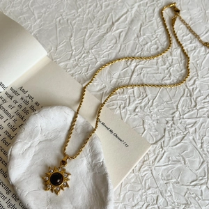 Collier pendentif tournesol en œil de tigre et acier titane or sur fond texturé blanc
