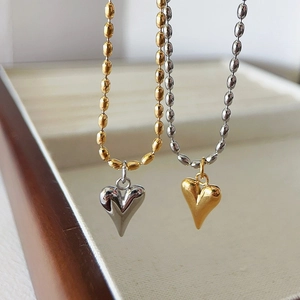 Two-tone gold and silver heart necklaces with beaded chains on a jewelry display tray