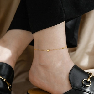 Close-up of a dainty gold ankle chain featuring a heart pendant worn with black loafers