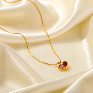 Collier élégant en titane doré avec pendentif cœur rouge foncé sur tissu en soie blanc