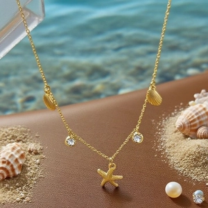 Détail du collier étoile de mer et coquillages dorés avec cristaux sur le sable