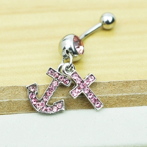 Detailed close-up of pink crystal navel ring with anchor and cross charms on wood