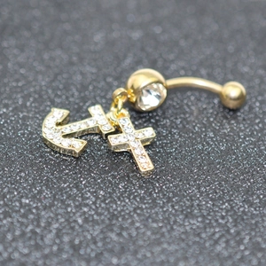 Macro shot of gold navel ring with crystal-encrusted cross and anchor charms