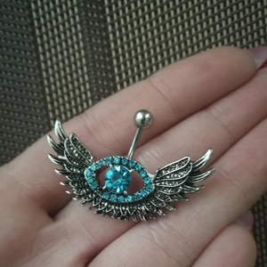 Detailed close-up of a winged eye belly button ring with blue crystal rhinestones