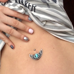 Silver belly button ring with angel wings and a blue stone on a woman's navel