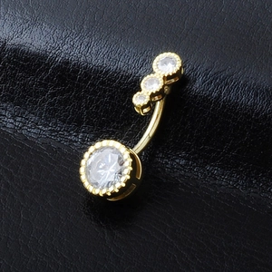 Detailed macro view of gold-plated navel ring with four cubic zirconia stones on leather