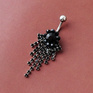 Dangle flower belly ring with black crystals and silver tassels on a textured surface