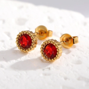 Gros plan de boucles d'oreilles en zircon rouge avec bords dorés sur pierre texturée blanche