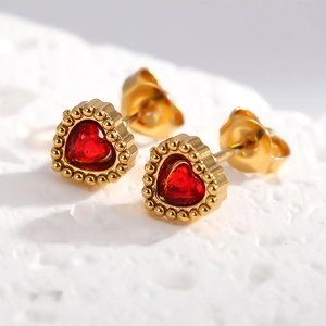 Vue macro détaillée de puces d'oreilles cœur en or avec zircon rouge et bords perlés